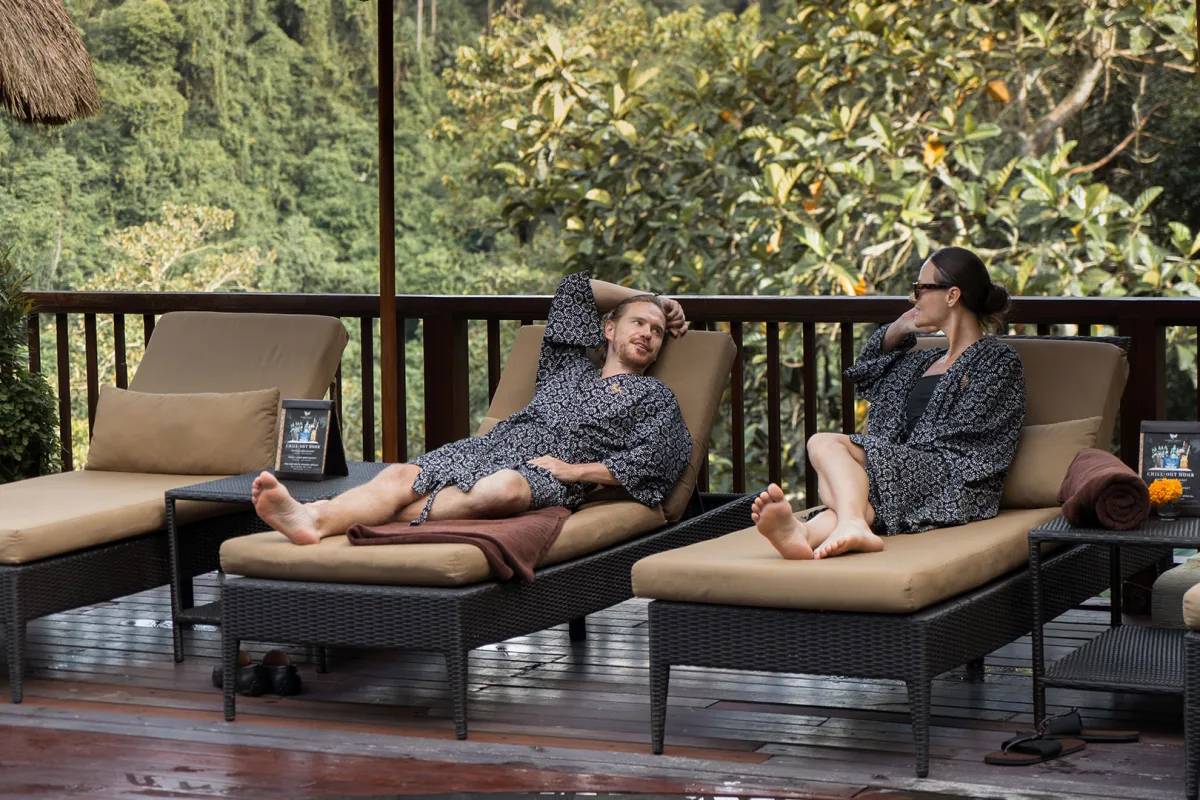 Two guests relaxing on outdoor sun loungers overlooking the lush tropical jungle at Kamandalu Ubud, Bali.
