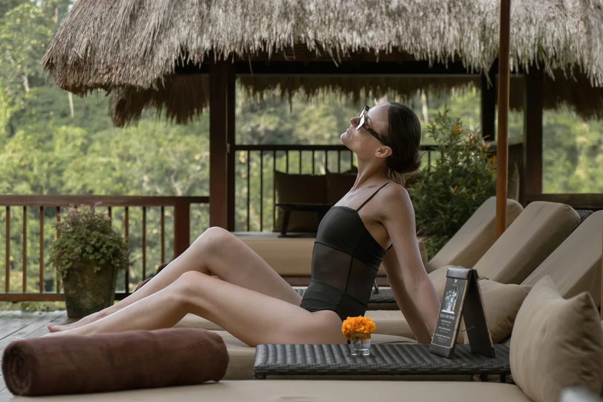 Woman relaxing on a sun lounger overlooking the lush tropical jungle at Nandini Jungle by Hanging Gardens, Bali.