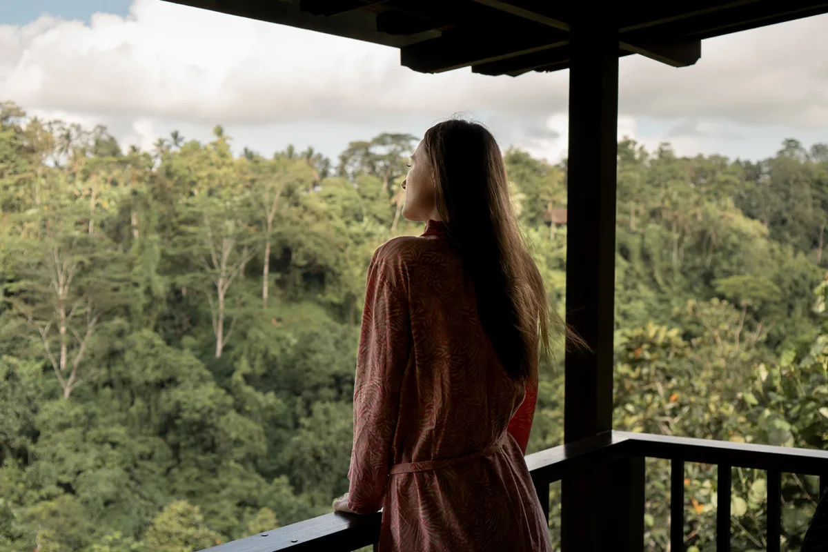 Solo female traveler enjoying peaceful views of the lush tropical jungle from a private villa balcony at Nandini Jungle by Hanging Gardens in Ubud, Bali.