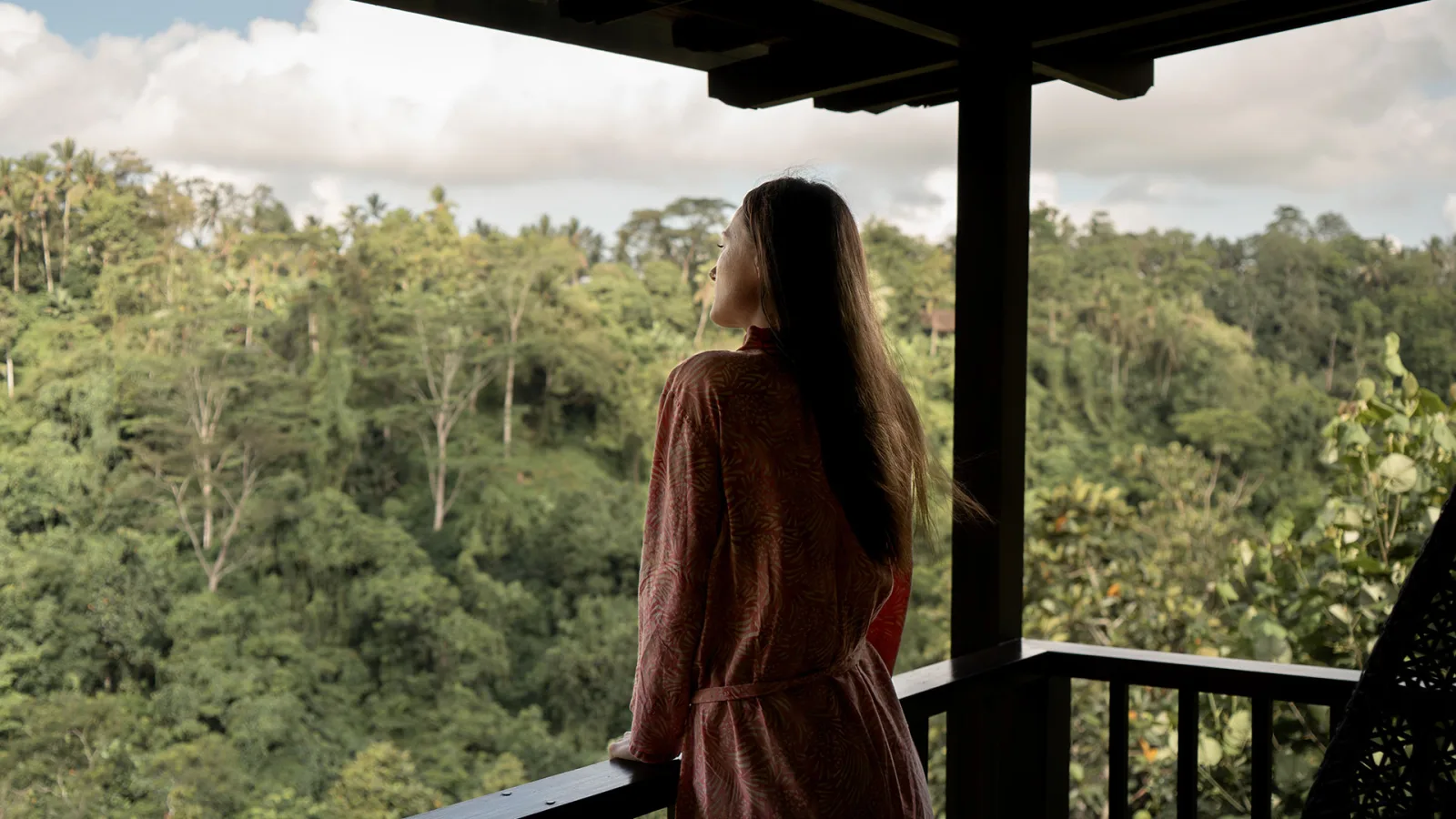 Solo female traveler enjoying peaceful views of the lush tropical jungle from a private villa balcony at Nandini Jungle by Hanging Gardens in Ubud, Bali.